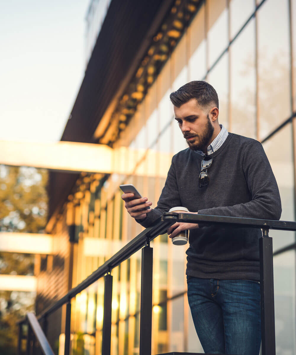 Person leaning against railing outside of building looking at phone