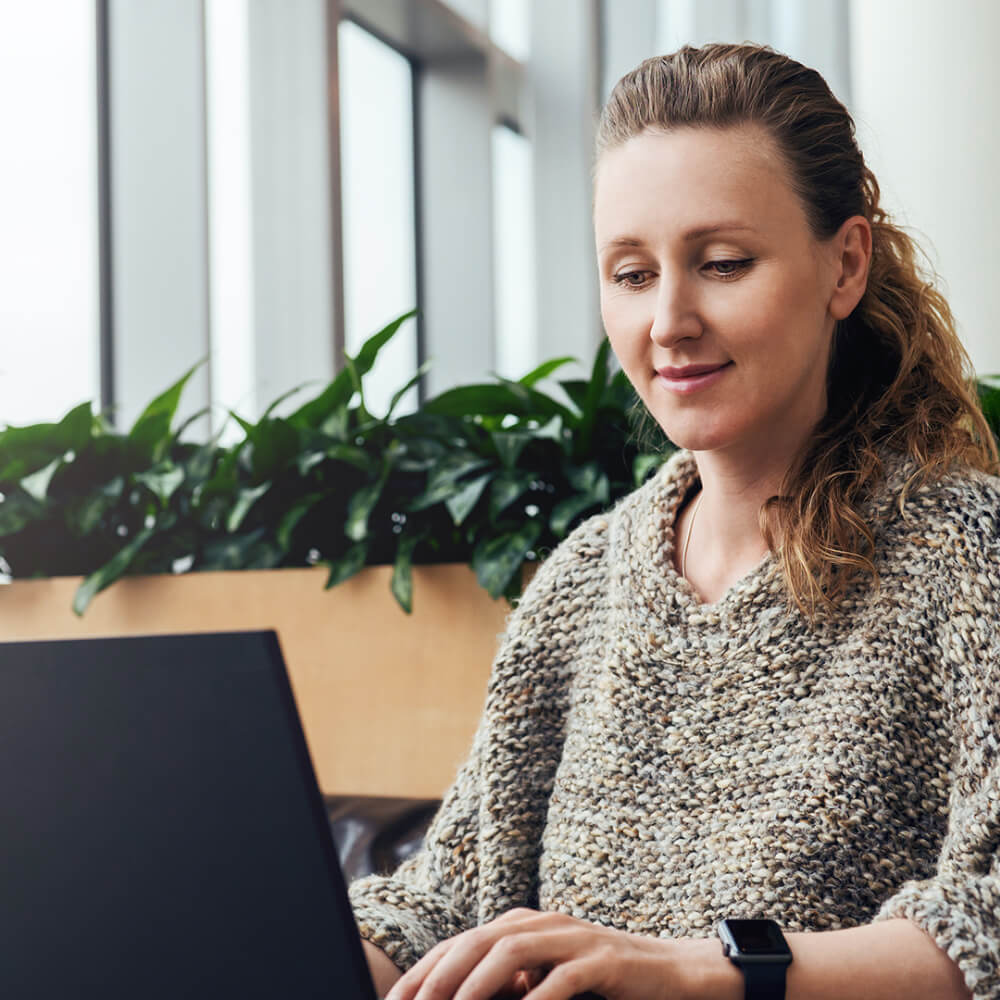 Person working on laptop at table with greenery background