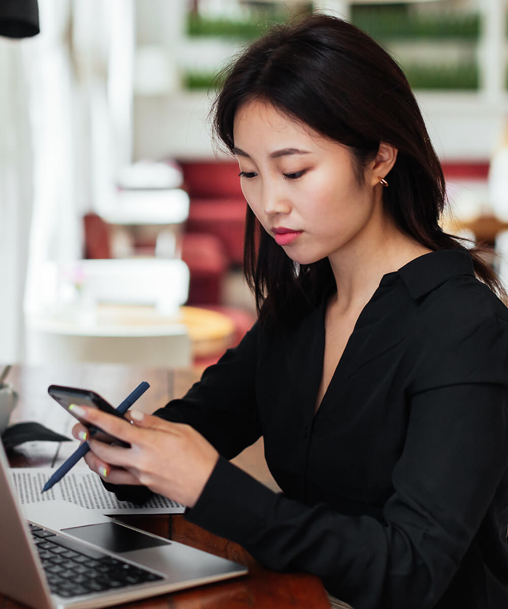 Person sitting at desk working on laptop looking at phone
