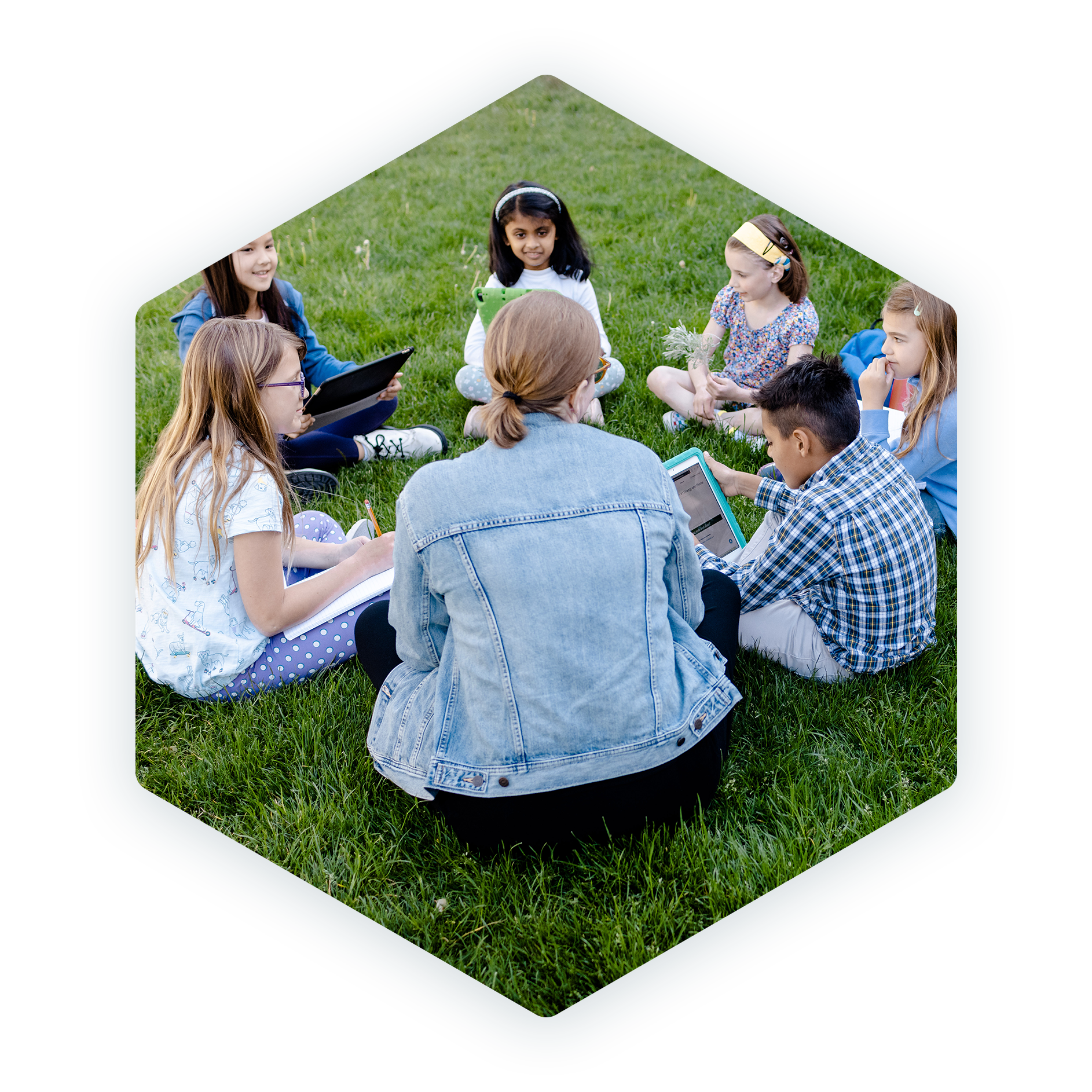 A teacher and students forming a circle and sitting on the grass