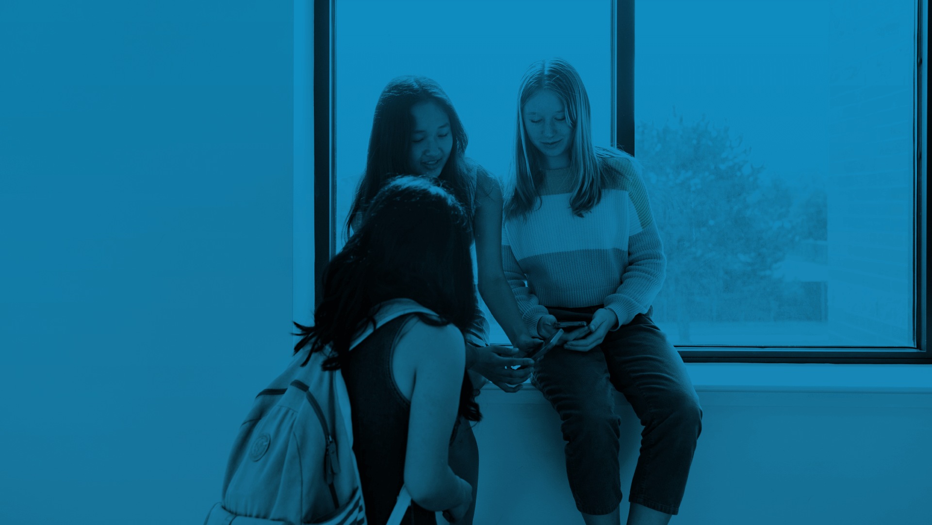 A group of students sitting on a window sill looking at their cellphones