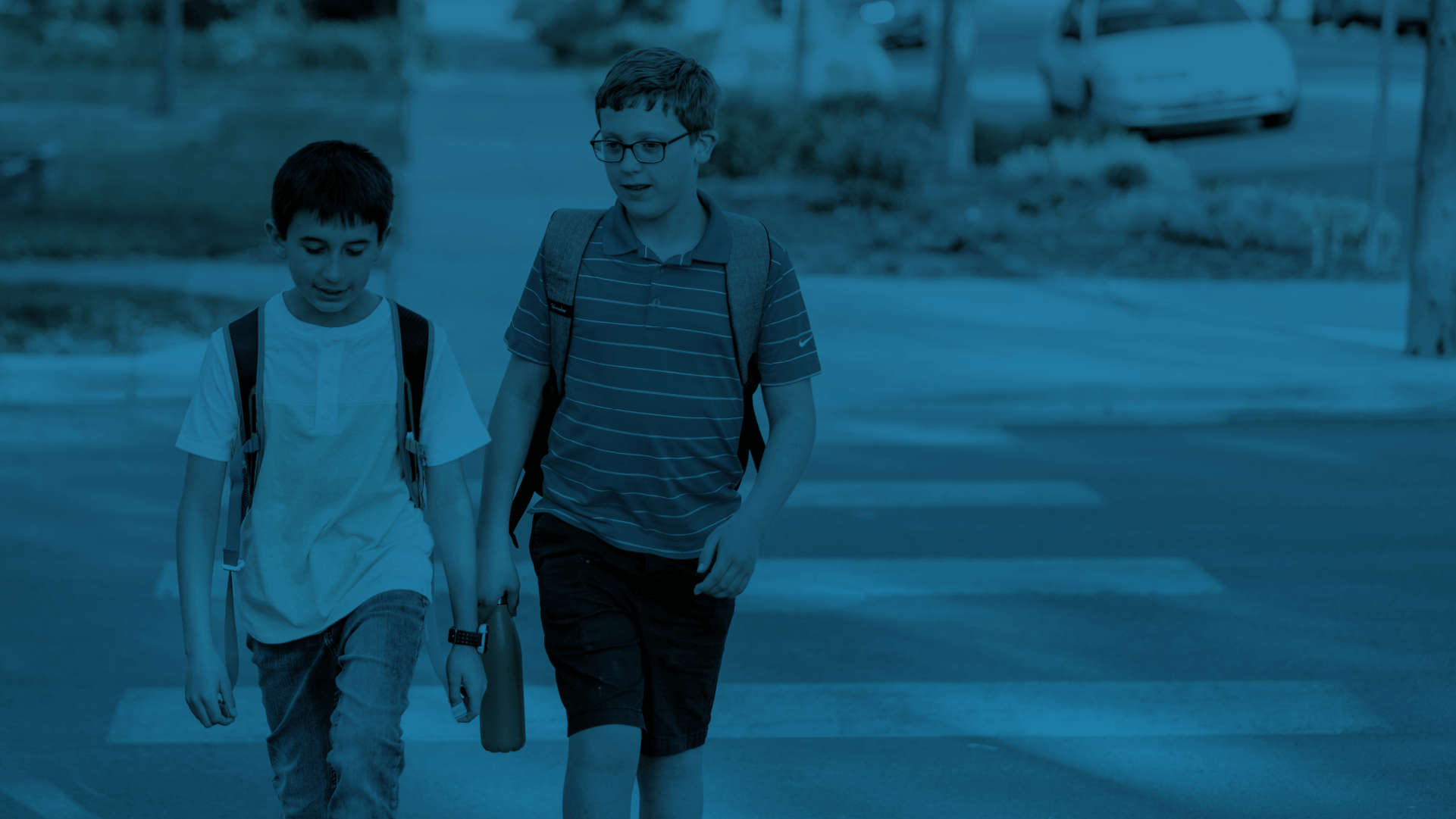 Two students wearing a backpack while crossing the pedestrian lane