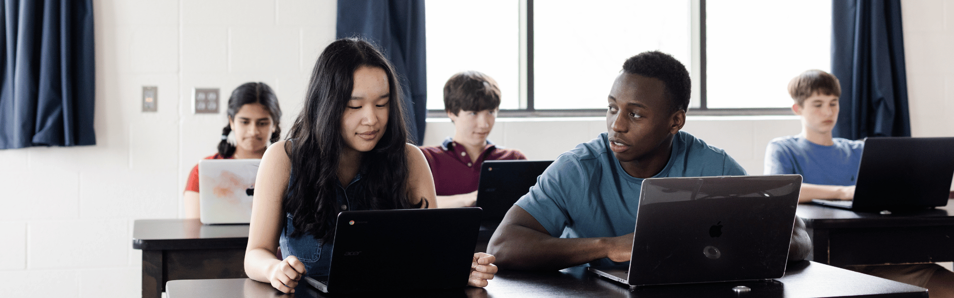 two students sitting at a desk, looking at laptops during a lesson