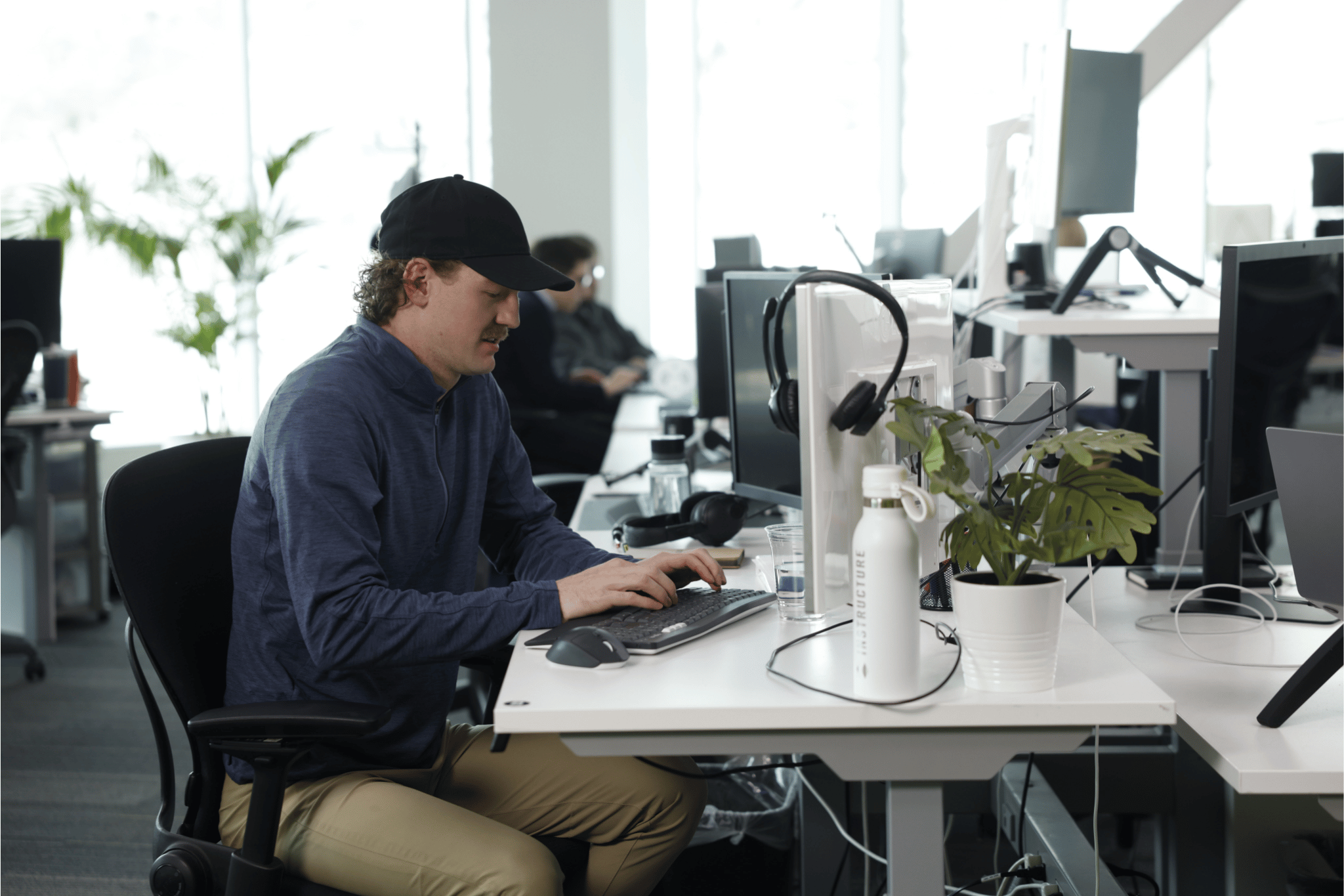 Young man sits at desk in front of computer in a sunny office