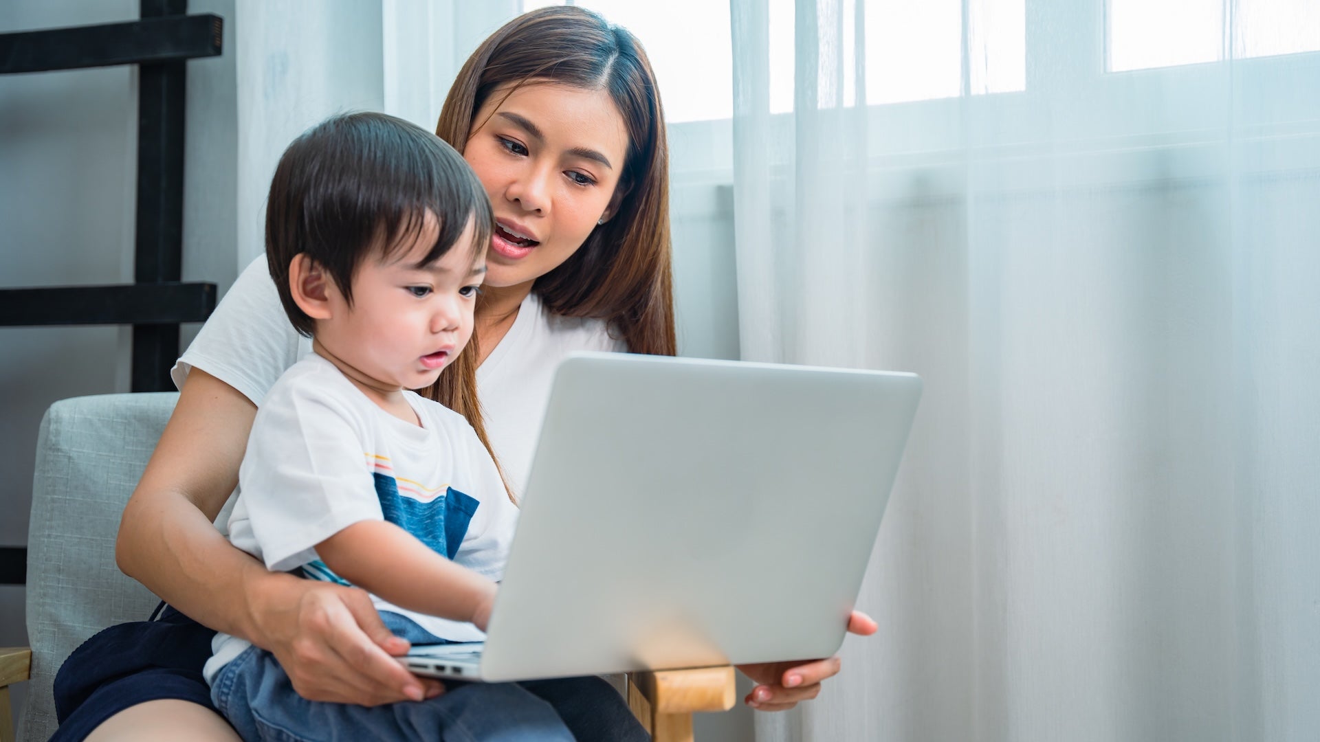 Woman sits in a chair with an open laptop and a toddler on her lap