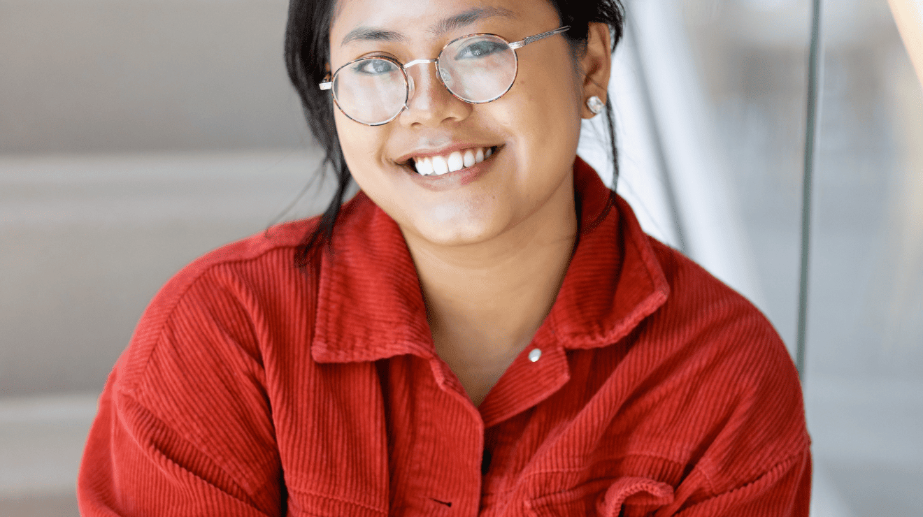 A woman wearing glasses and a red shirt, smiling and looking towards the camera.
