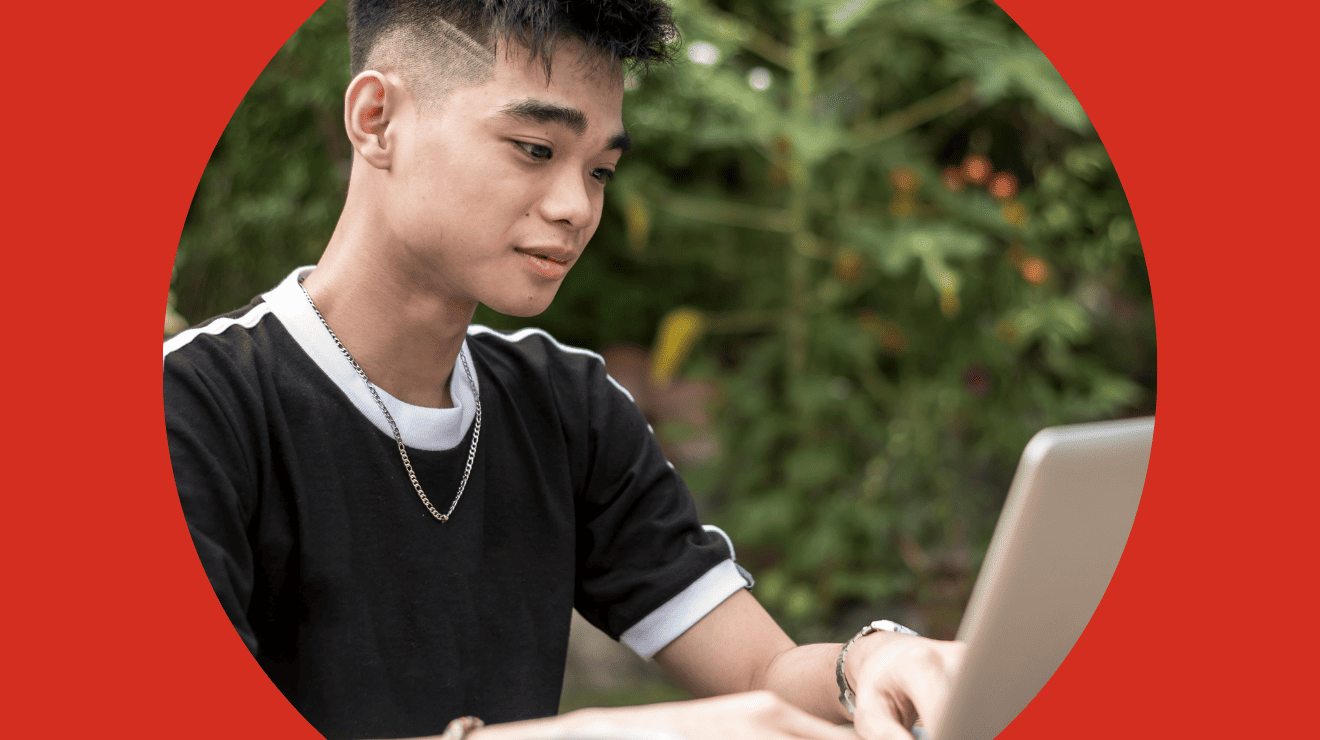 A young man sits in front of a laptop, focused on the screen while working or studying.