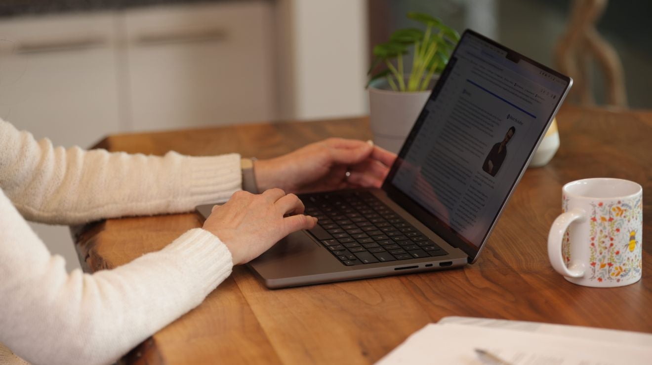Remote employee reading course content on a laptop at a kitchen table.