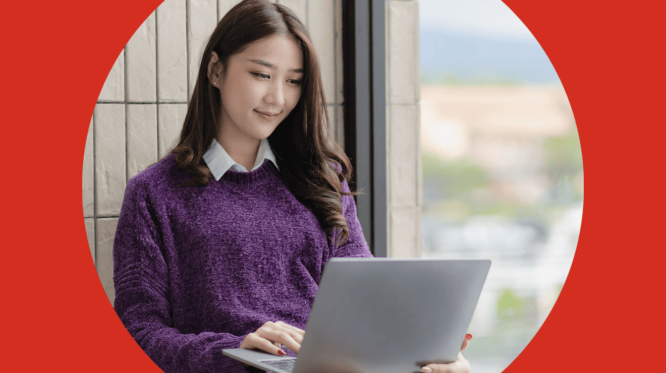 A woman sitting on a bench, focused on her laptop, surrounded by greenery in a park setting.