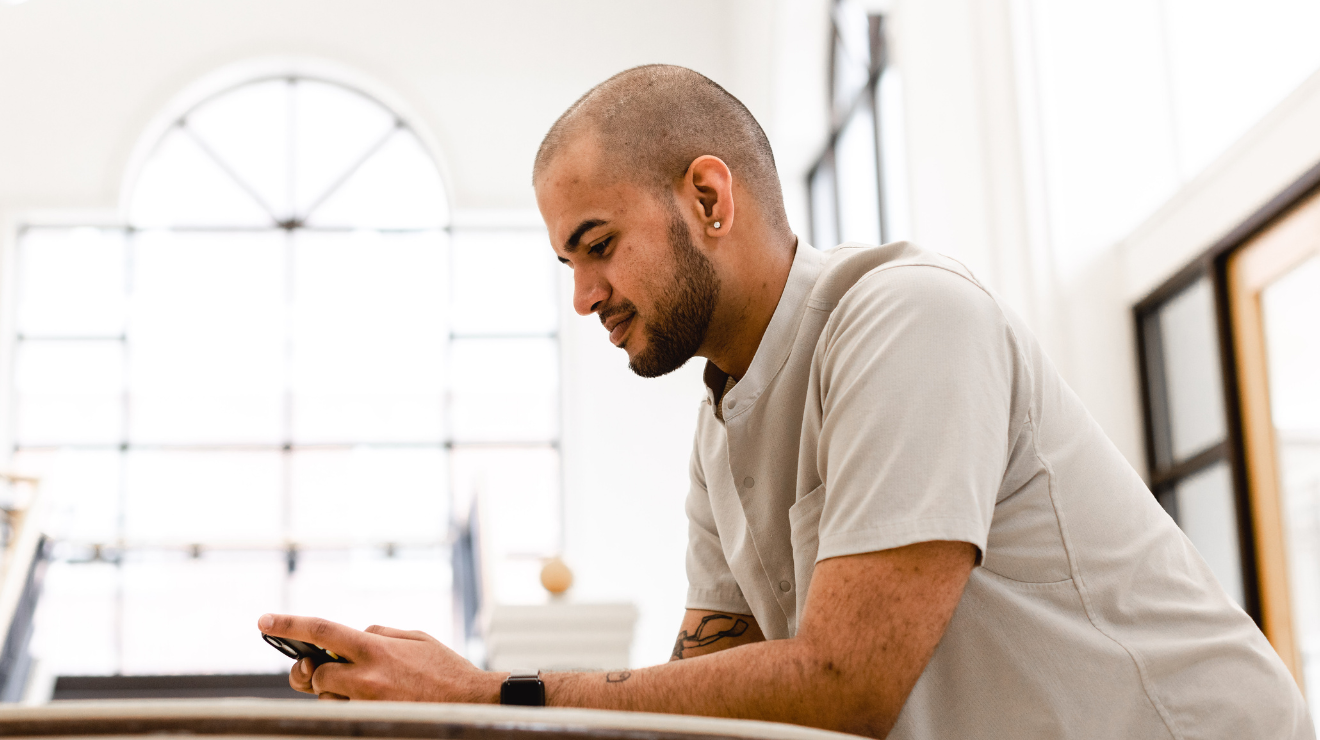 A man sitting on a couch, focused on his phone, with a relaxed expression.