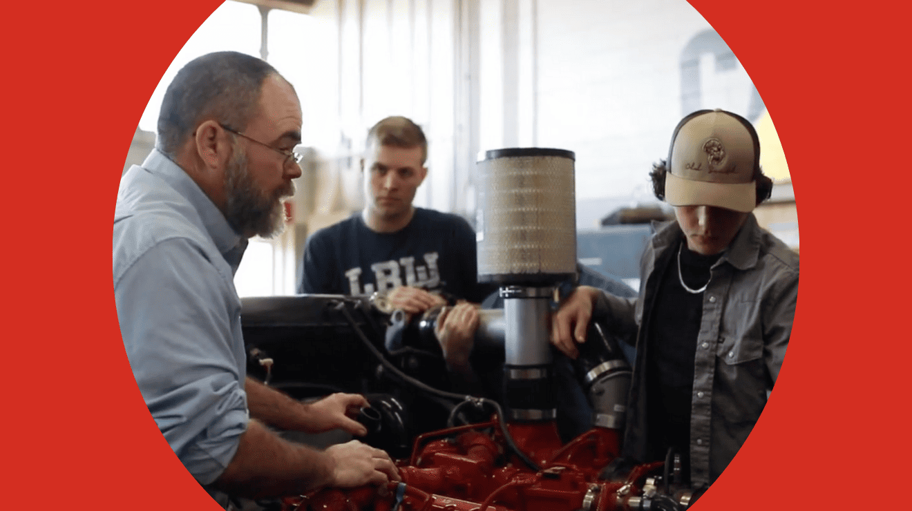 Two men repair a red engine in a workshop, surrounded by tools and equipment.