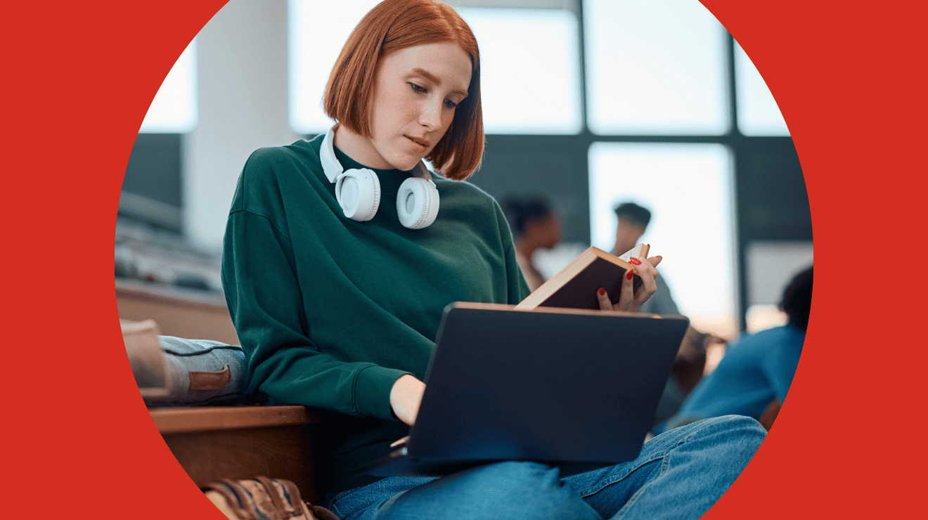 A woman wearing headphones sits on a bench, focused on her laptop in an outdoor setting.