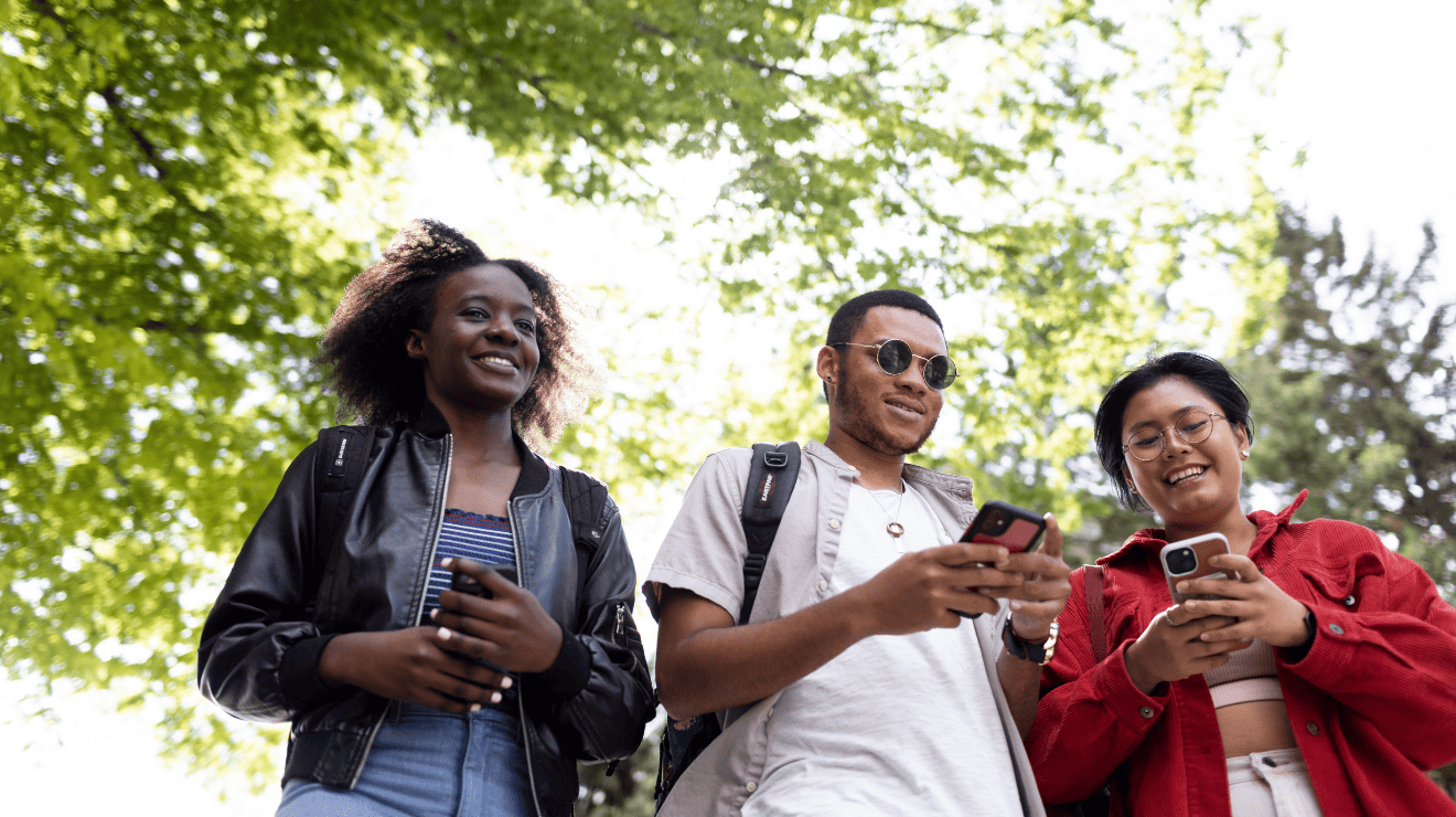 Three young people in a park, each focused on their phones, surrounded by greenery and sunlight.