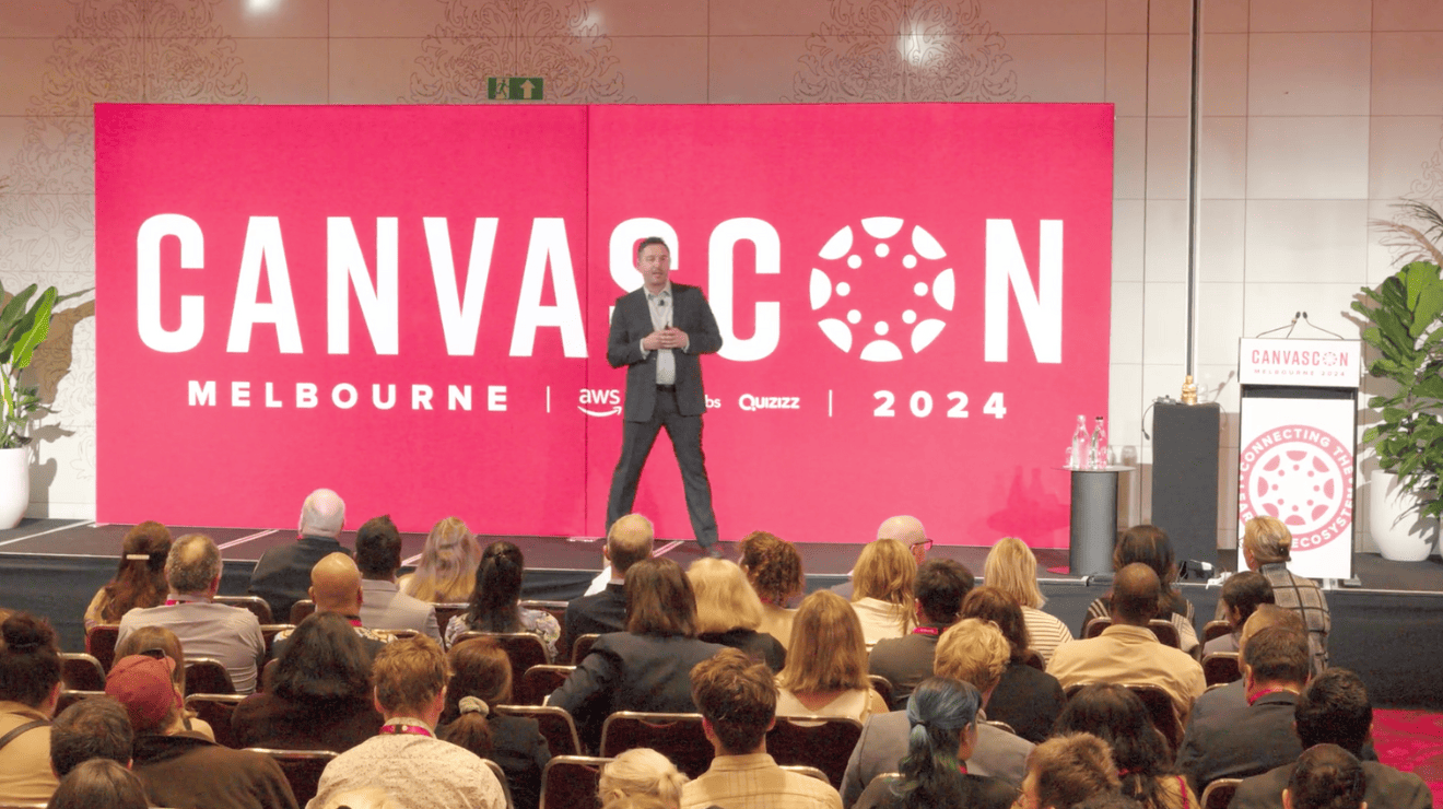 A man presenting at a conference, standing at a podium with a projector screen in the background.