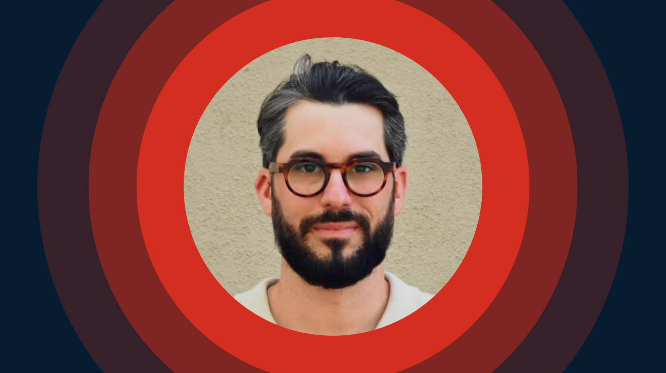 A man with glasses and a beard with red circles as a background.