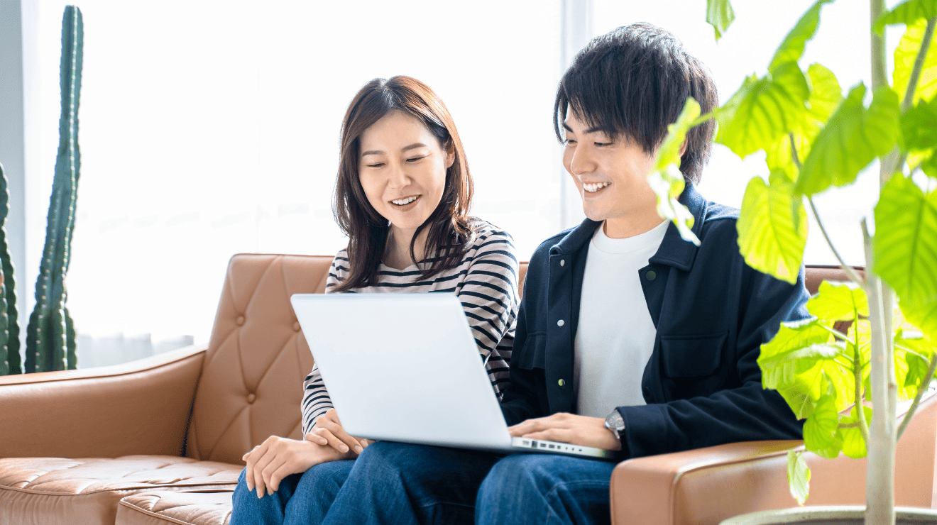 A couple is seated on a couch with a laptop, appearing engaged and comfortable in their shared digital activity.