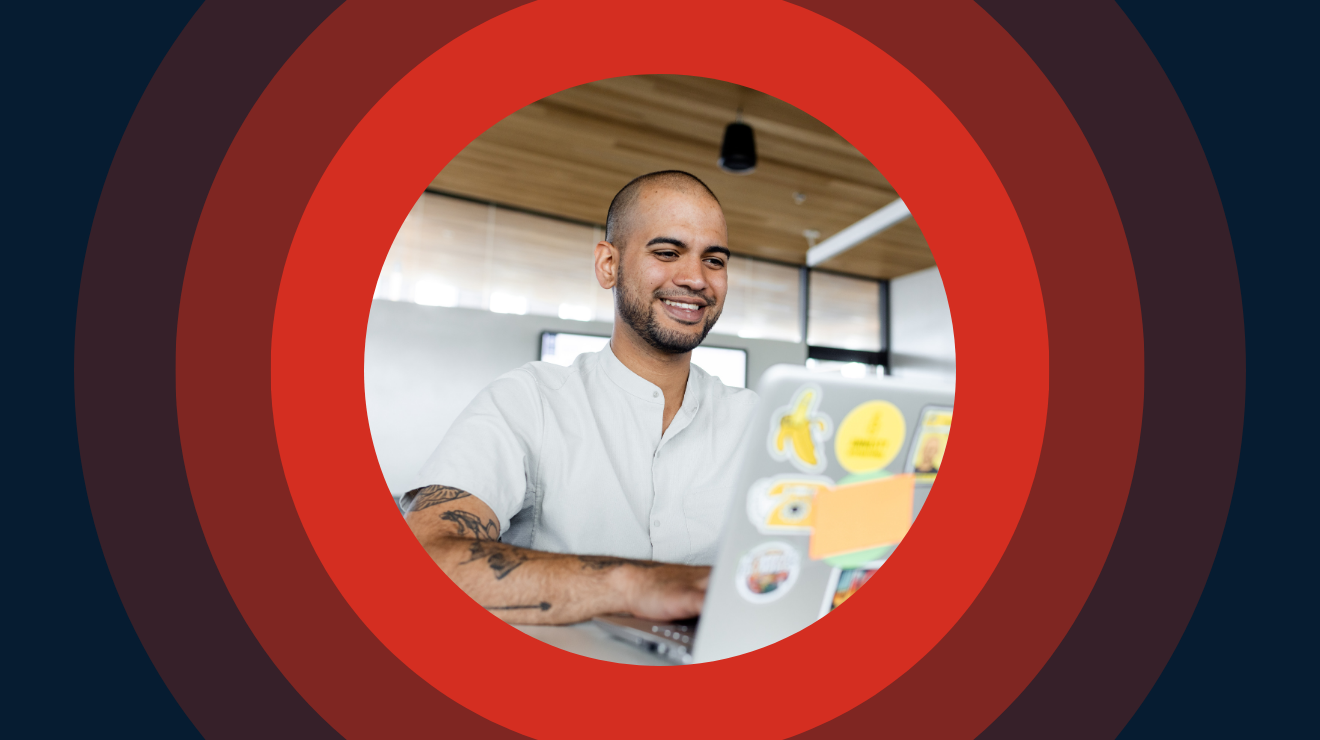 A man in a white shirt sits at a desk, working on a laptop.