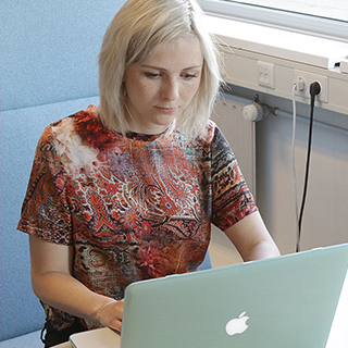 A woman seated at a desk, focused on her work with a laptop and notepad in front of her.