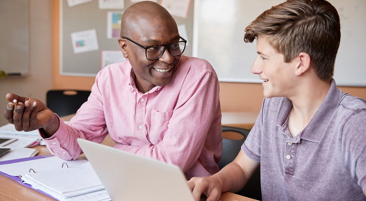 A student and teacher reviewing course work on a laptop