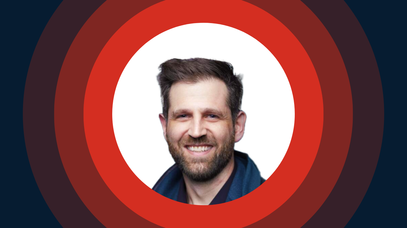 A smiling man with a beard wearing a blue shirt, exuding a friendly and approachable demeanor.