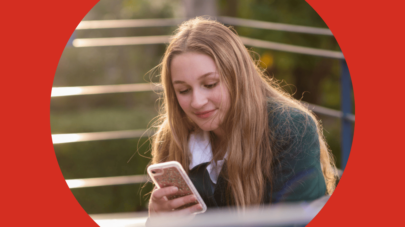 A girl sits outside, focused on her phone, surrounded by greenery and sunlight.