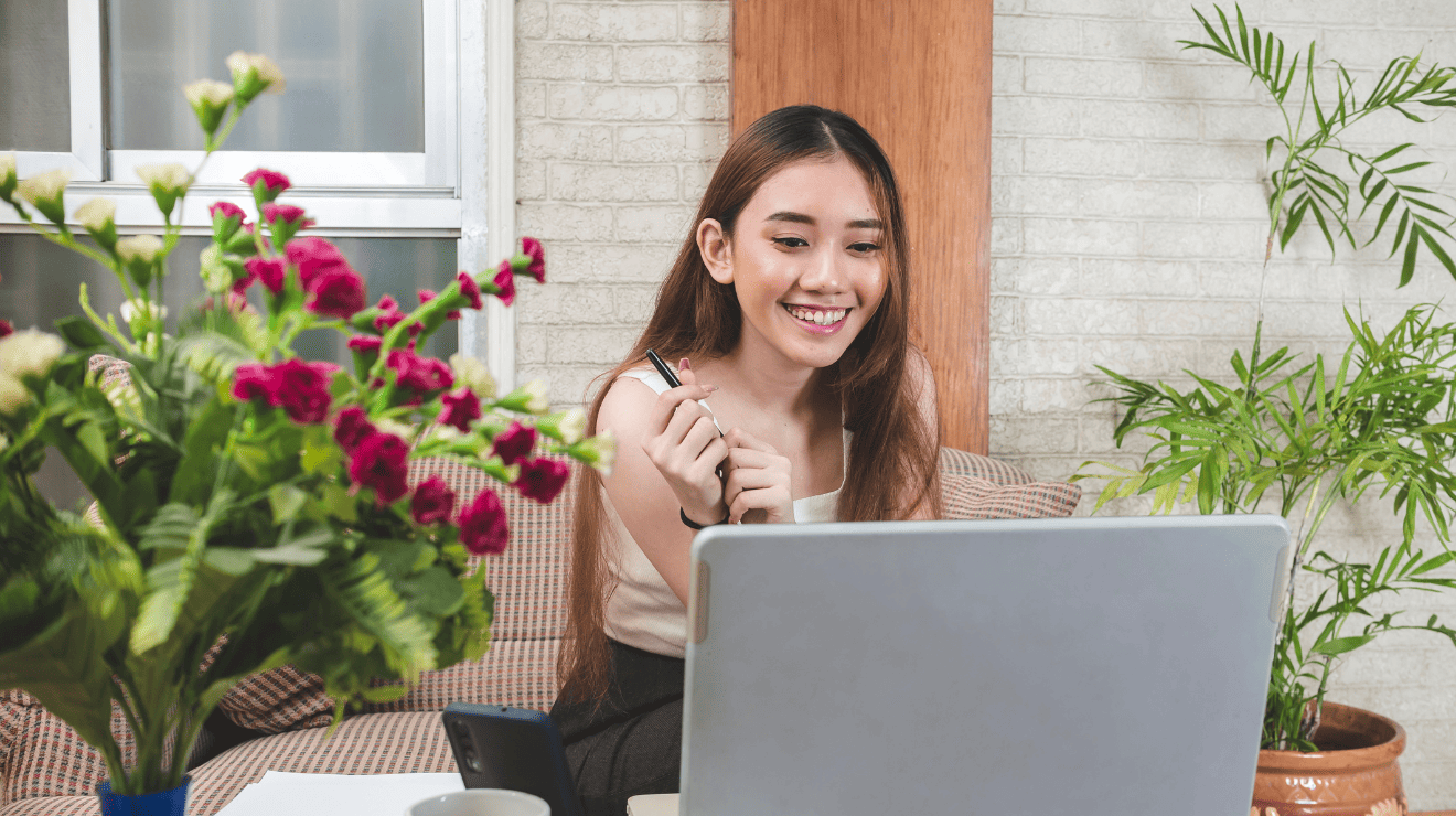 A woman smiles while working on her laptop, conveying a sense of joy and engagement in her task.