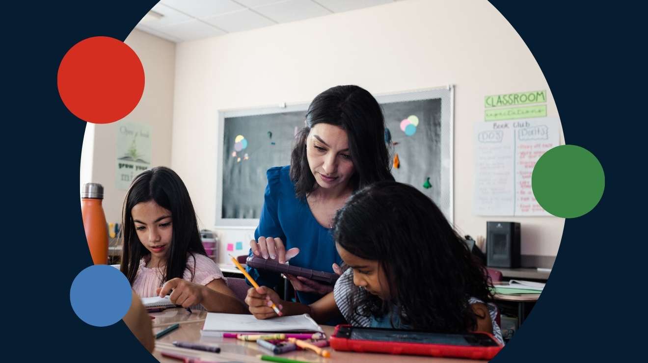 a teacher puts data into a tablet next to two students at a table