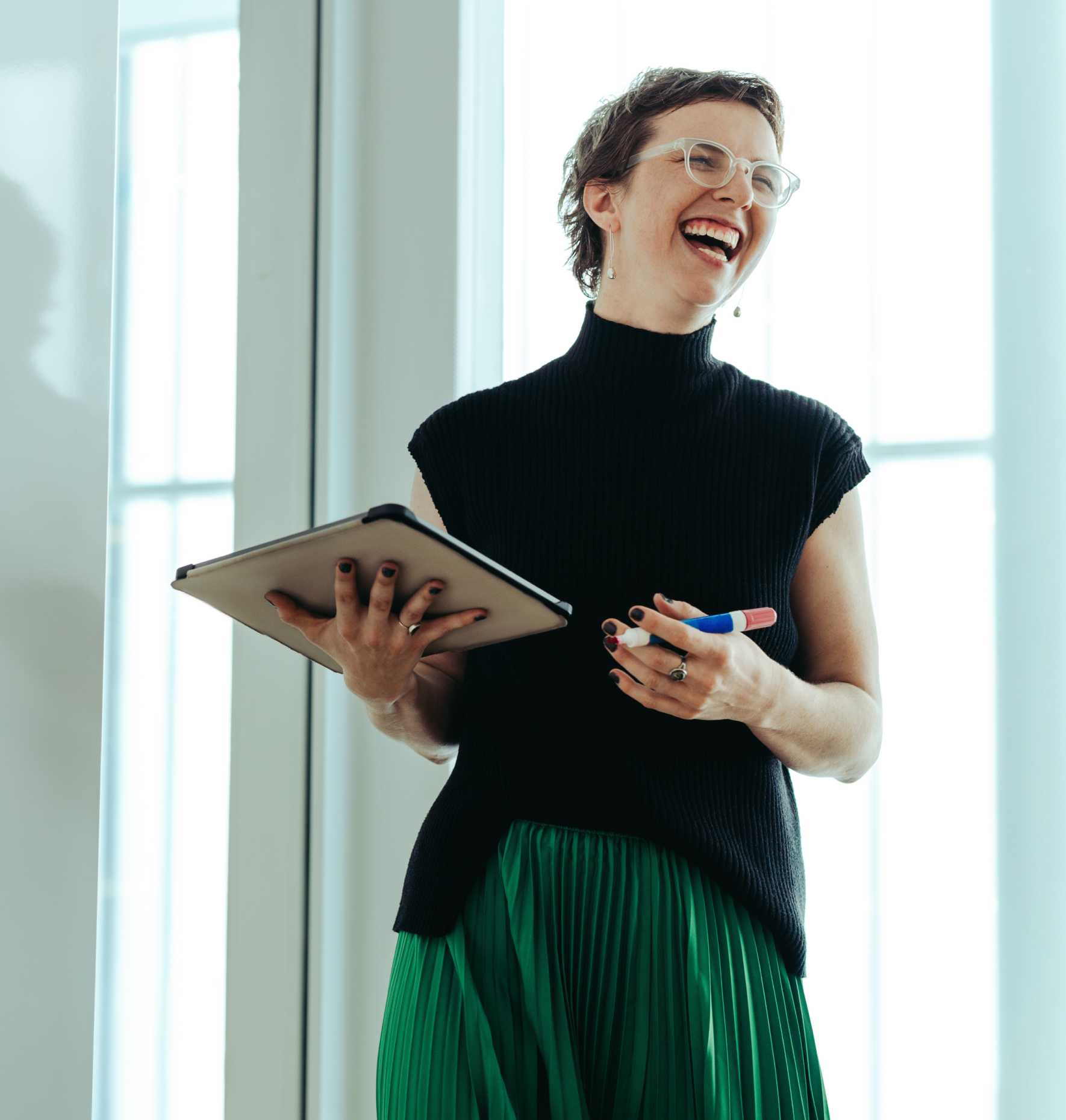 A woman laughing and holding a tablet.
