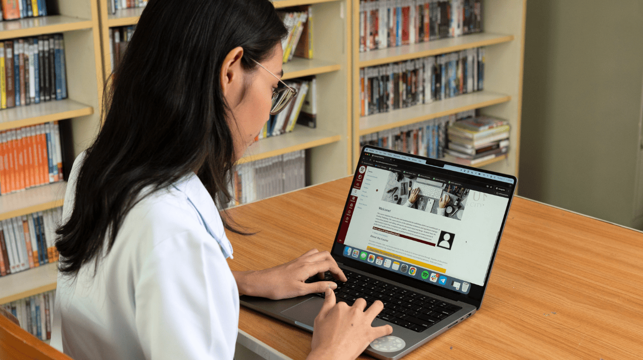 Young woman sits at library table with laptop open and Canvas displayed