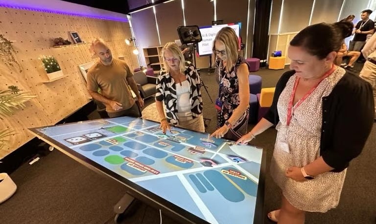 Student and teachers around a touch screen, interacting with an illustration of a map.