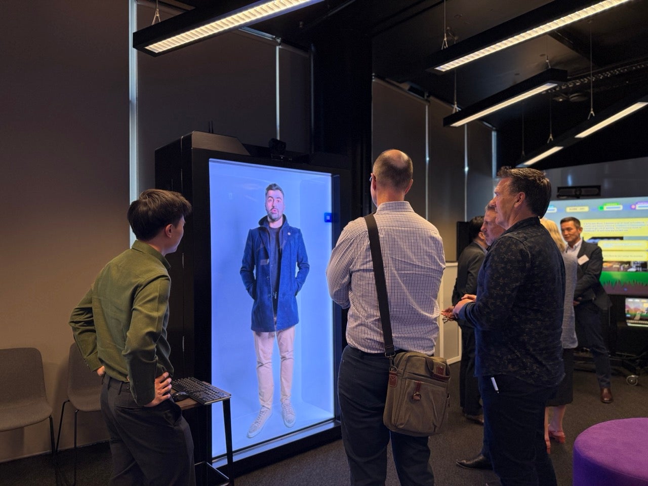Three people around a Digital Human on a real-size screen. 