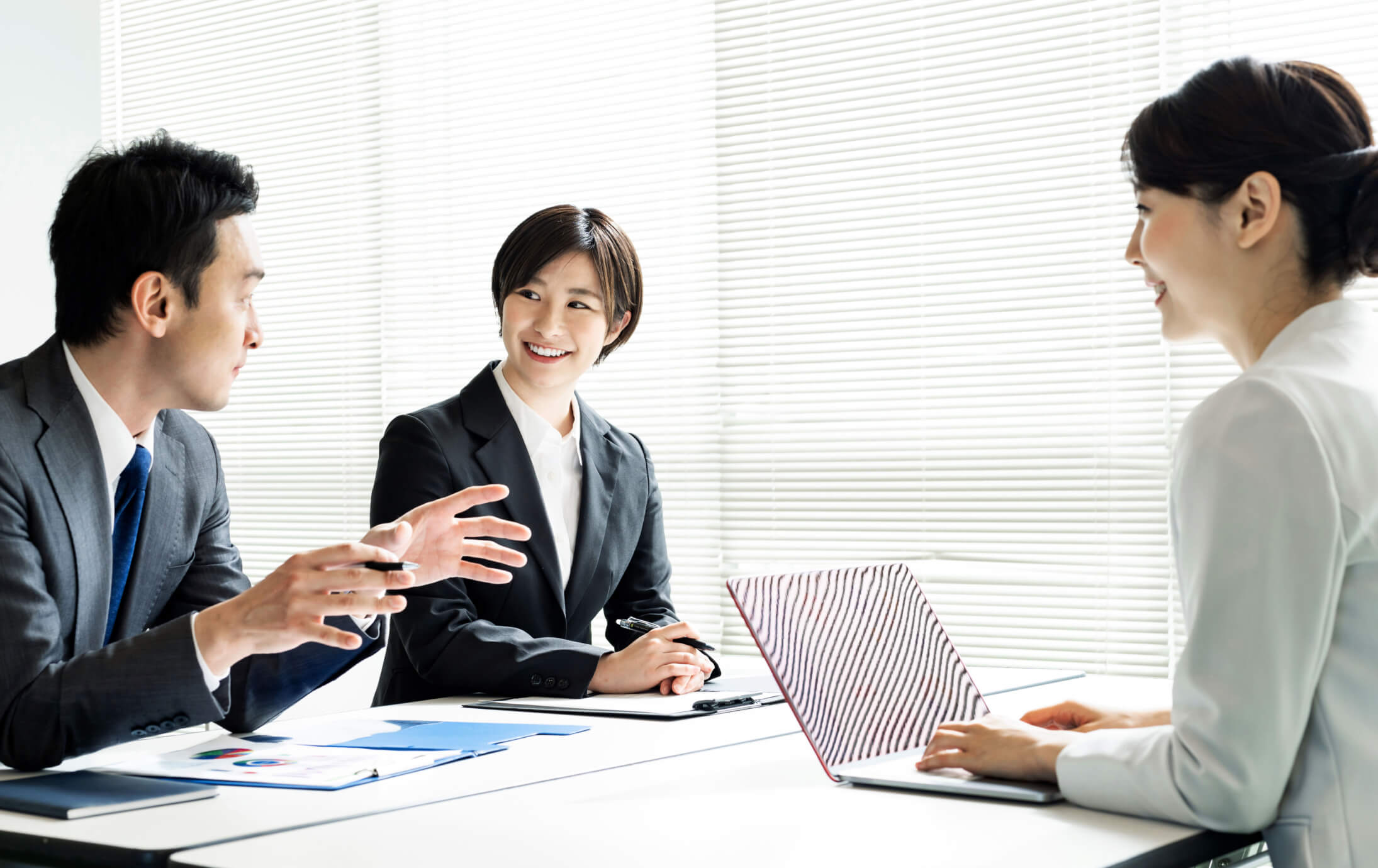 Three co-workers smiling and laughing around a conference table.