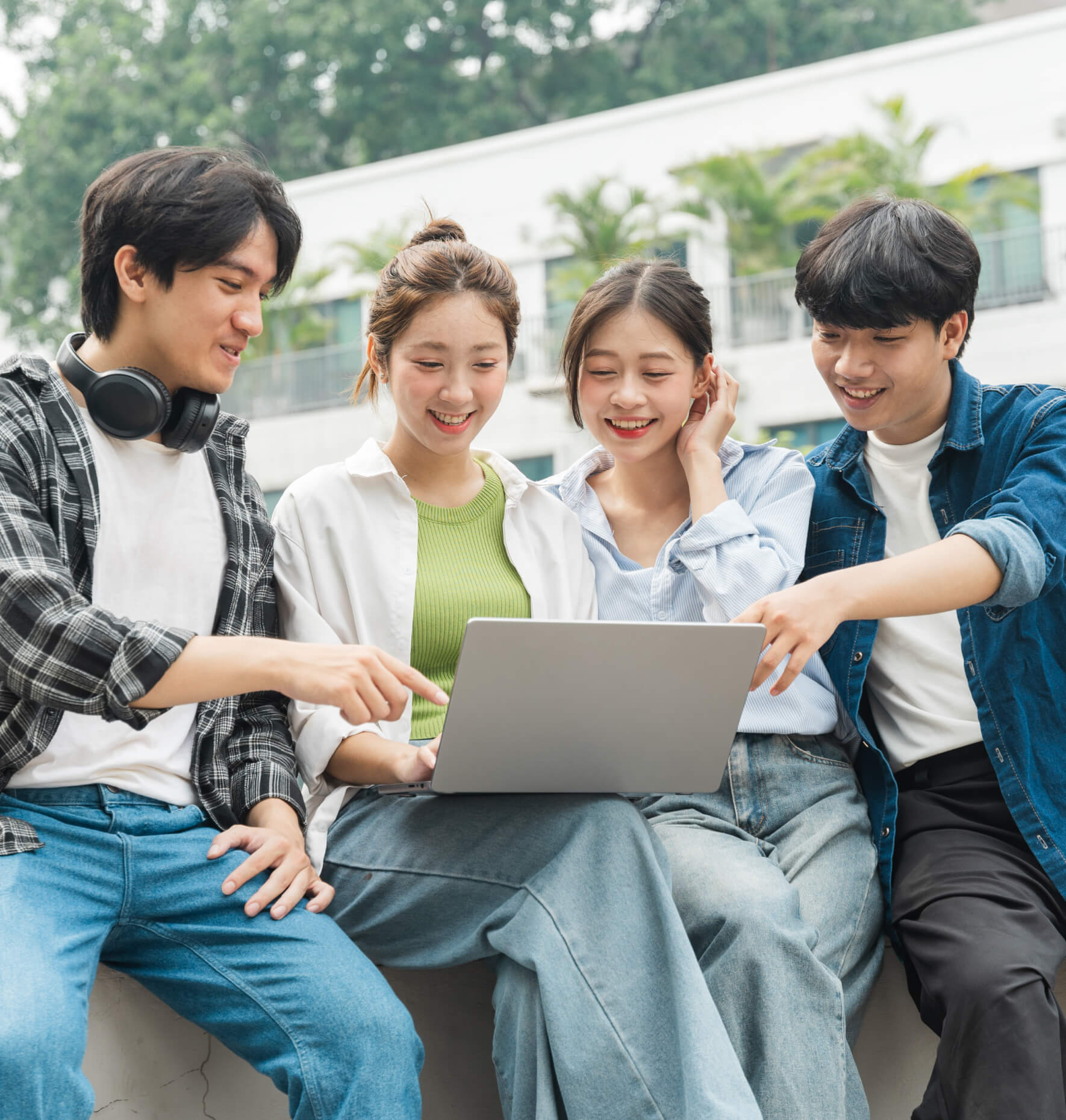 Four students smiling and sharing a laptop