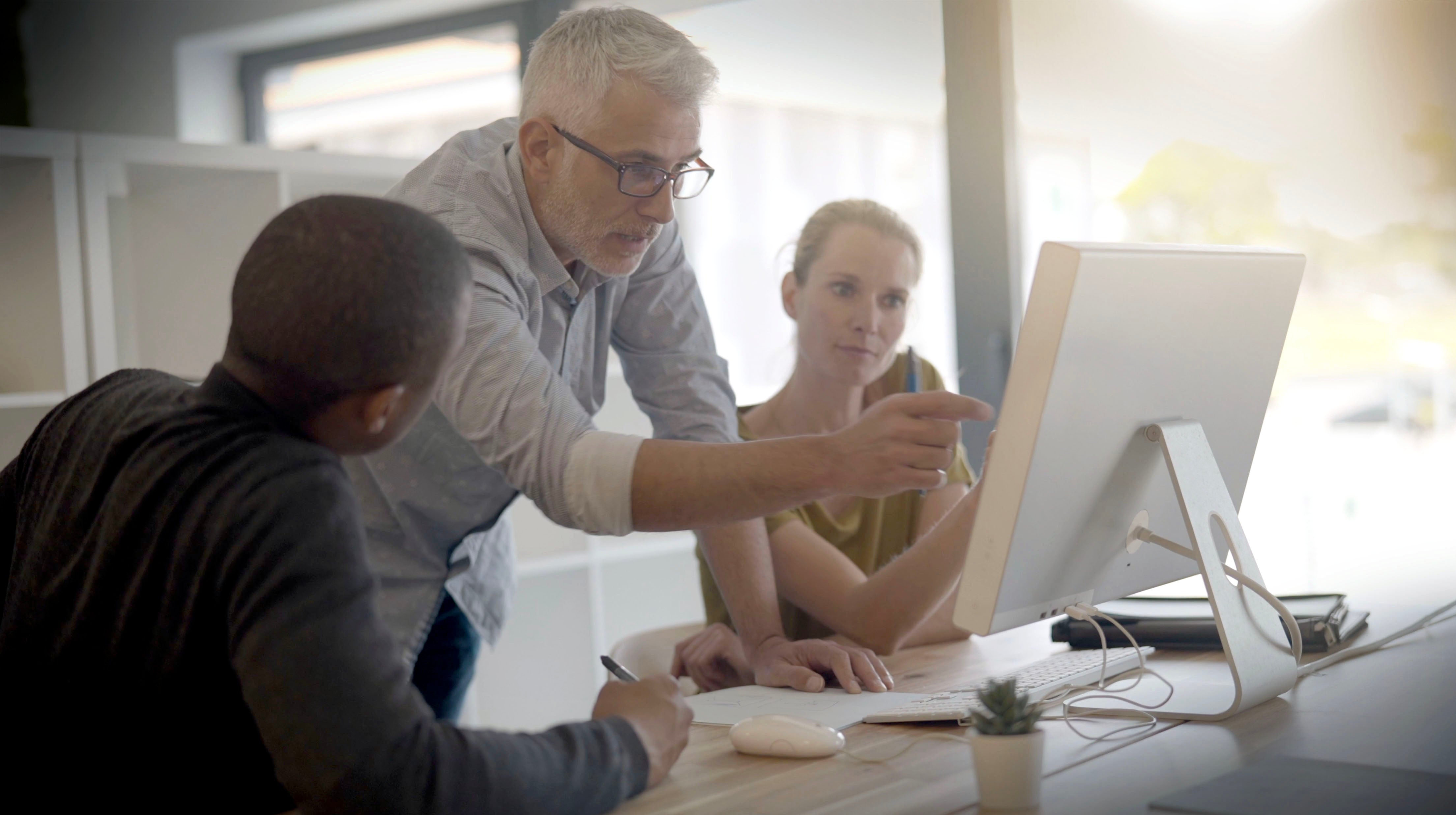 Guy pointing at computer while two employees look on
