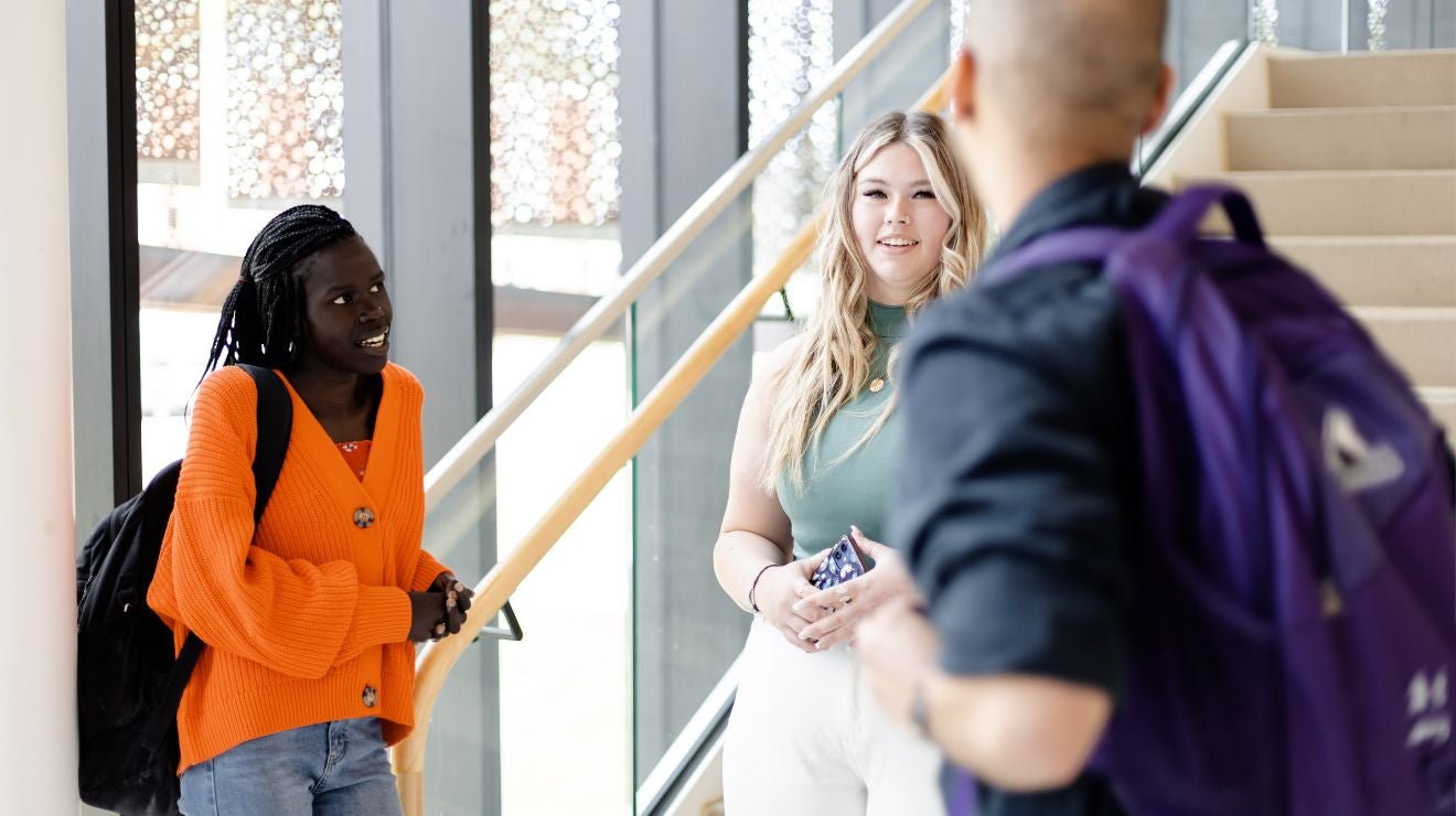 3 adults standing in a circle near a staircase, looking at each other in conversation
