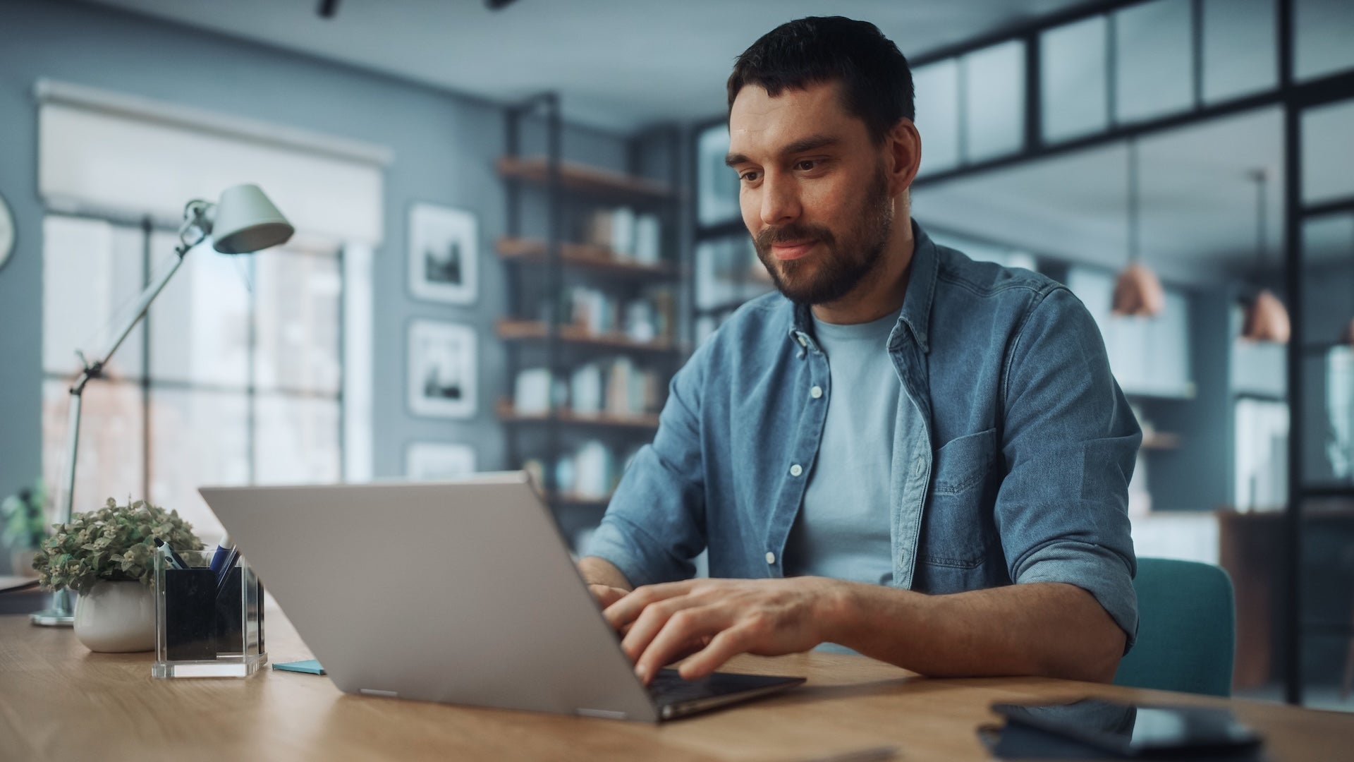 A man works on a laptop at a desk in a modern office.