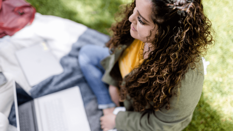 Student sitting in grass with laptop and notebook