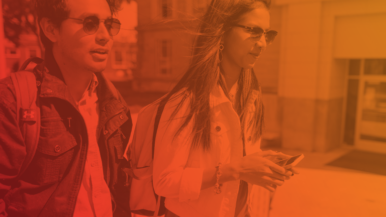 Two students wearing sunglasses walking through a street.