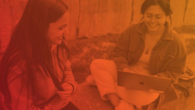 two girls sitting in the grass on their laptop. image has a red overlay