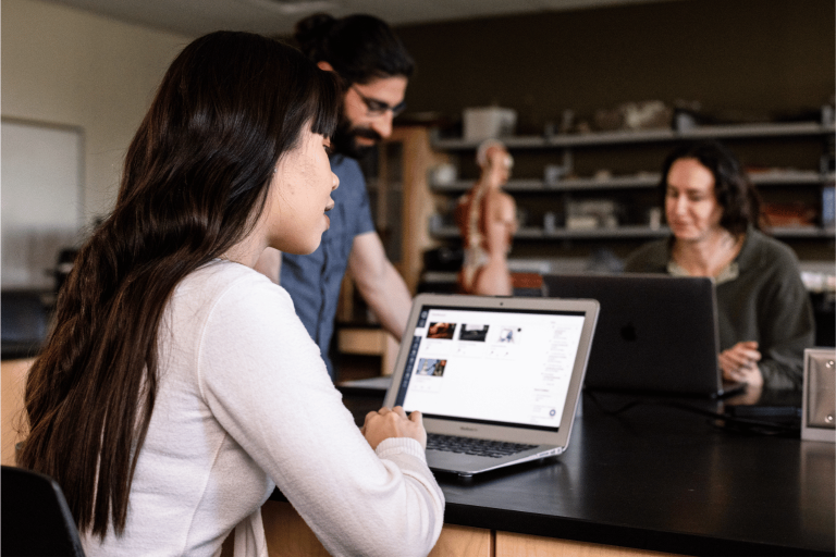 Students sitting at a desk looking at Canvas on a laptop