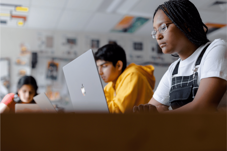 students sitting at a desk, looking at computer during class