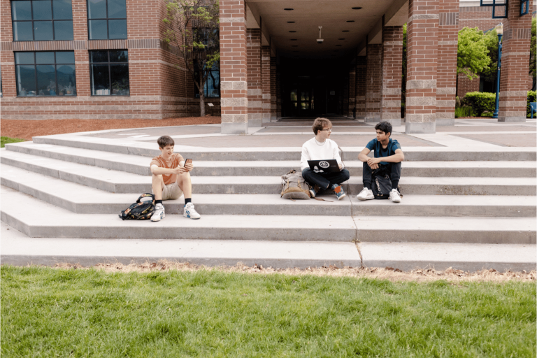 image of three k-12 students sitting on school steps using an LMS on their laptops