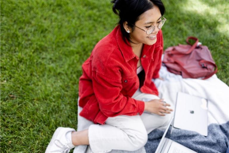 student sits with laptop in the grass