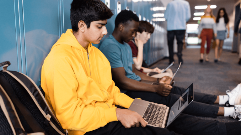 A group of students seated in a hallway, each using a laptop for study or collaboration.