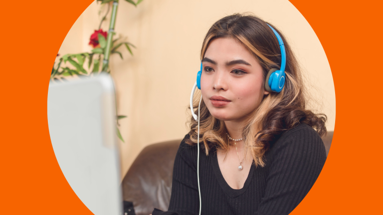 A woman wearing headphones sits in front of a laptop, focused on her work or a virtual meeting.