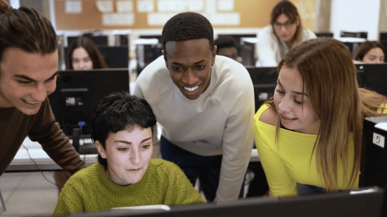 A group of students focused on their computers while collaborating in a classroom setting.