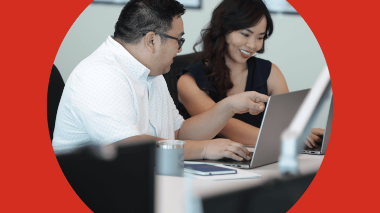 A man and woman seated at a desk, focused on a laptop, engaged in a discussion or collaboration.