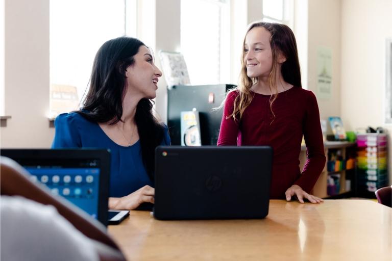 a teacher talks to a student at a laptop