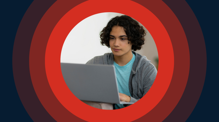 A young man in casual attire, sitting in front of a laptop, appearing concentrated on his work.