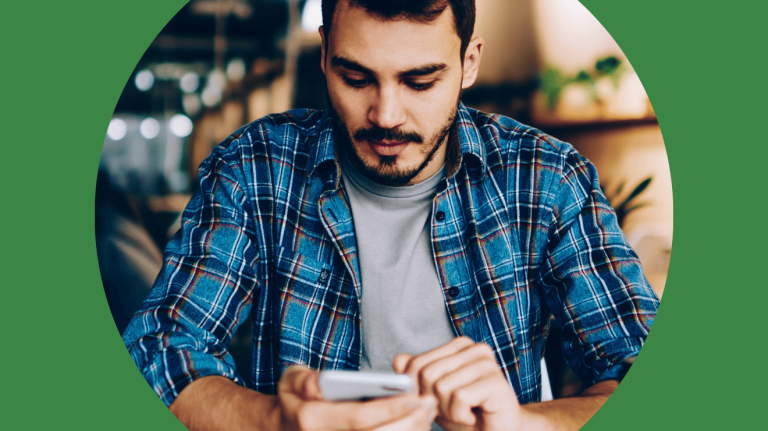 A man in a plaid shirt is intently looking at his smartphone, appearing focused on the screen.